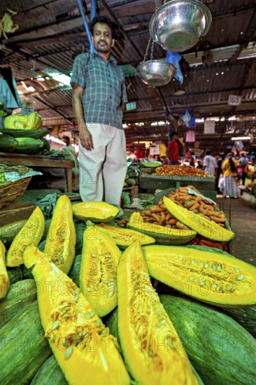A man stands at a market stall with glowing pumpkin and other fresh vegetables, The old market halls of Kandy in Sri Lanka