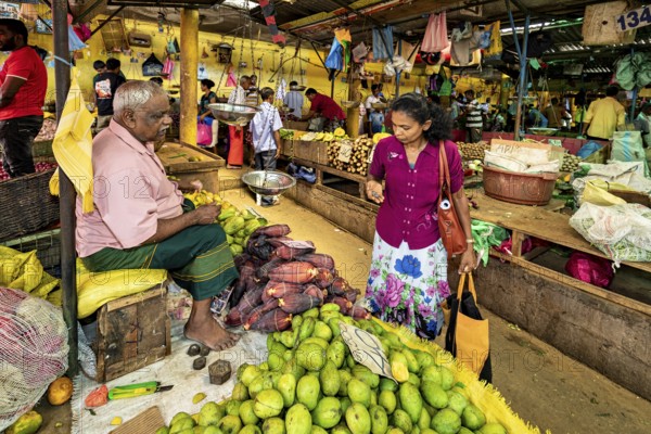 A man and a woman are discussing green mangoes at a colorful market stall, the old market halls of Kandy in Sri Lanka