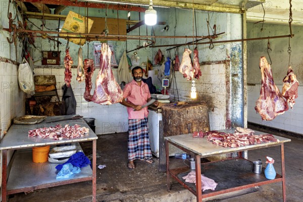 Butcher in traditional slaughterhouse with pieces of meat hanging on hooks, The old market halls of Kandy in Sri Lanka