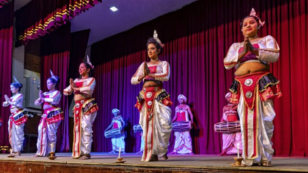Artists in colorful traditional clothing dance on a stage in front of a red curtain, folklore and dancers from the famous Kandy Dance in Kandy in Sri Lanka
