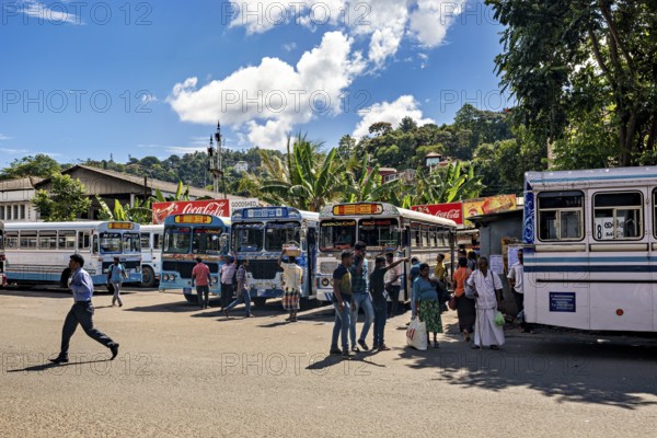 Buses park at a stop under tropical skies as people walk around, Kandy bus station in Sri Lanka