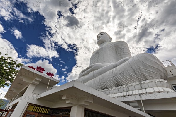 Large white Buddha statue under dramatic sky surrounded by temple architecture and clouds, white Buddha statue in a temple in Kandy in Sri Lanka