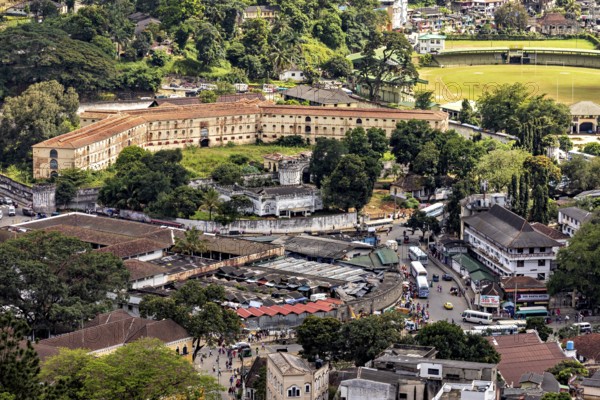 View of a historic fortress next to a lawn surrounded by city and trees, view of the city center of Kandy in Sri Lanka