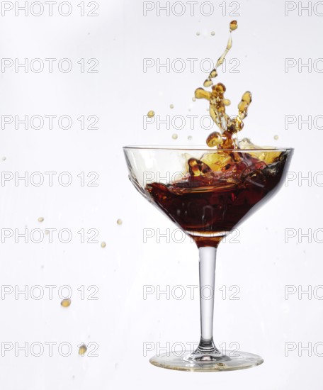 A brown liquid sloshes back and forth in a cocktail glass, studio shot against a white background
