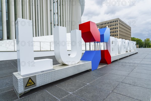 Exterior view of the Grande-Duchesse Joséphine-Charlotte Concert Hall on the Kirchberg Plateau in the European Quarter of Luxembourg City, Luxembourg, with surrounding modern high-rise office buildings. Contemporary architectural landmark photographed in daylight, featuring elegant columns, clean lines, and an urban business district atmosphere