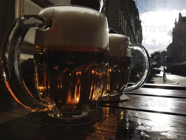 Beer mugs on a table at sunset with an urban backdrop in the background, Pilsen, Czech Republic