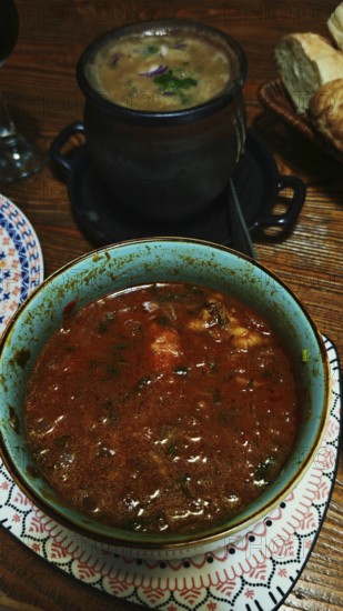 Green bowl with a delicious, rich red Georgian soup, Kharcho and a black pot in the background on a wooden table, Georgia