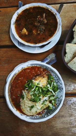 Two bowls of soup, Kharcho, served on a wooden table, one with chunky stew and the other with a red sauce topped with herbs, Georgia