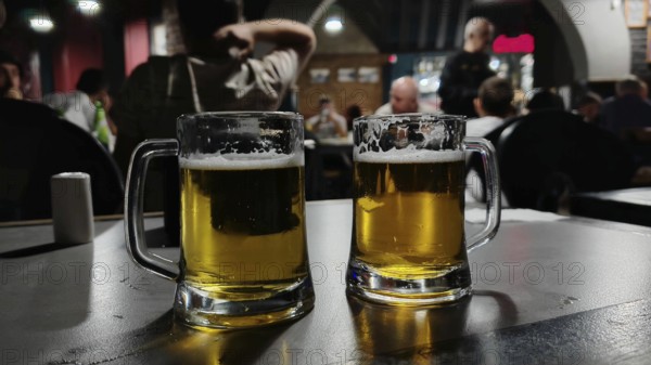Two beer glasses on a table in a bar with people in the background at dusk, Georgia