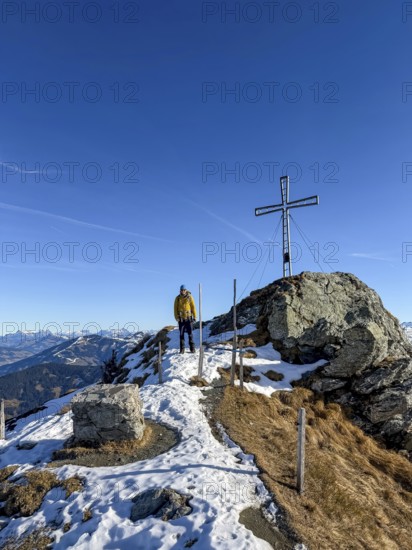 Hiker next to summit cross at summit of Feldalphorn, winter hiking, Kitzbühel Alps, Tyrol, Austria