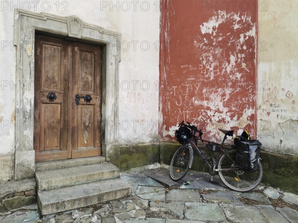 A bicycle parked in front of an old wooden door in a weathered church wall, Czech Republic