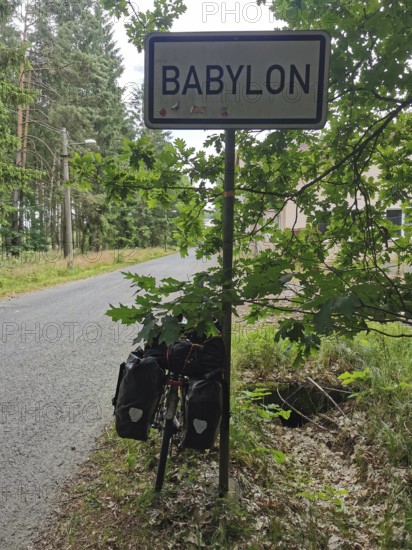 Bicycle with luggage bags in front of a Babylon town sign on a road through the forest, Czech Republic