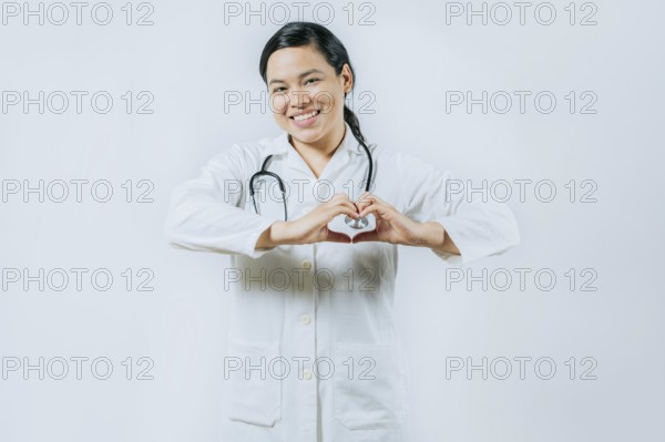Smiling asian female doctor making heart shape isolated. Asian healthcare worker gesturing heart