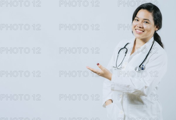 Smiling asian female doctor showing empty space isolated. Young asian doctor presenting something isolated