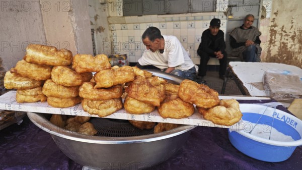 Fried pastries on a market stand surrounded by people in a street area, southern Morocco