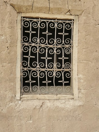 Decorated window screen in a crumbling, beige clay wall with rustic ambiance, Morocco