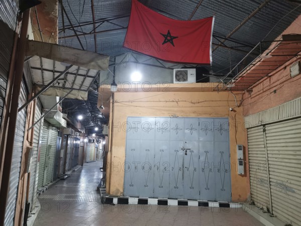 Medina during Ramadan Empty market alley at night with locked shops and a Moroccan flag, Morocco