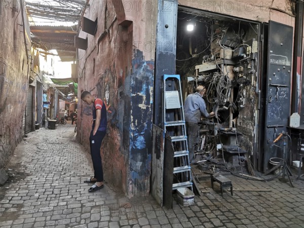 A man leaning against a wall in front of a chaotic workshop in the Medina, atmospheric picture, Morocco