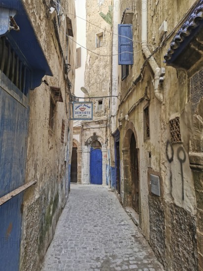 Narrow old town alleyway with weathered doors and the sign of a dentist, dentist, under a blue sky, Essaouira, Morocco