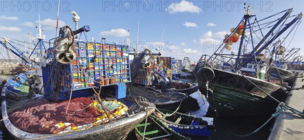 Fishing boats with colorful boxes and nets in quiet harbor under blue sky, Essaouira, Morocco