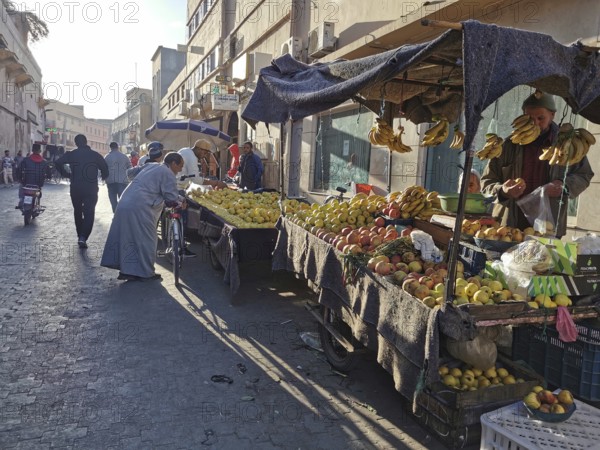 Bustling market street with stalls full of fresh fruit and people shopping, Morocco