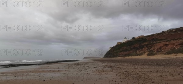 Empty beach with cloudy sky and rocky coast in the background, Morocco
