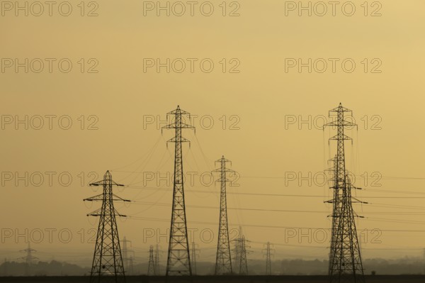 Electricity pylons and power lines silhouette at sunset, England, United Kingdom