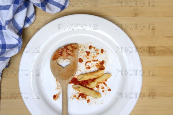 Plate with cooking spoon and leftovers from pasta, food waste