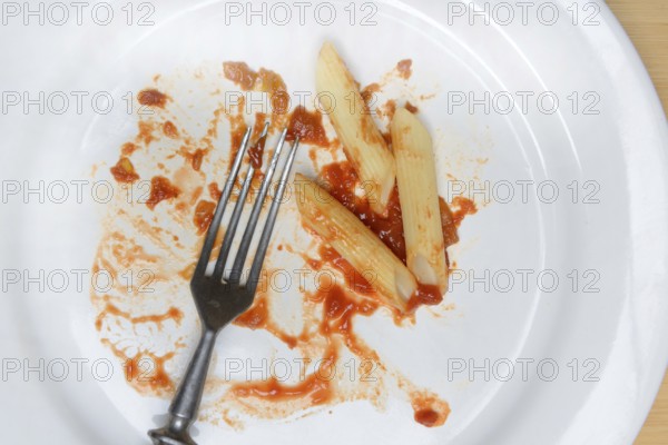 Plate with fork and leftover pasta, penne and tomato sauce, food waste