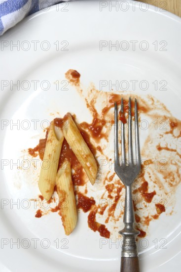 Plate with fork and leftover pasta, penne and tomato sauce, food waste