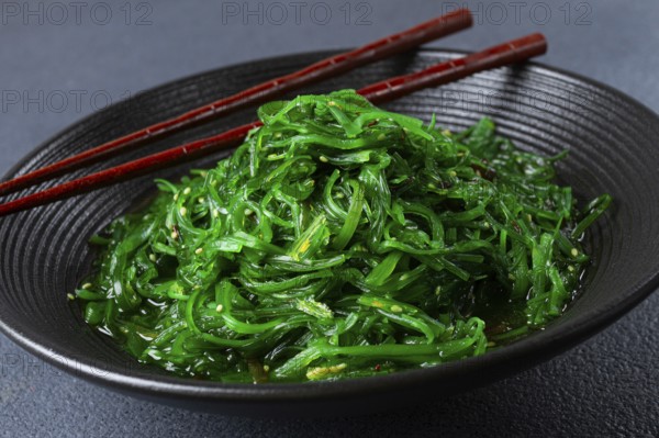 Chuka salad, made from fresh seaweed, with sesame dressing, served in a black bowl, with chopsticks