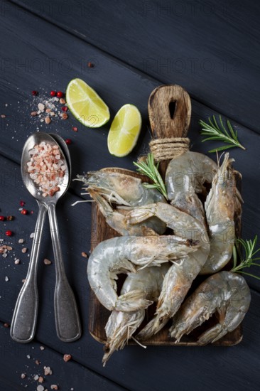 Fresh raw, white-footed shrimp, tiger prawns vannamei, on a wooden cutting board, with lime slices, and seasonings