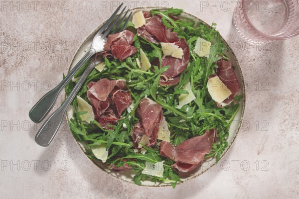 Fresh arugula salad with prosciutto and grated parmesan cheese, on a plate, homemade, no people