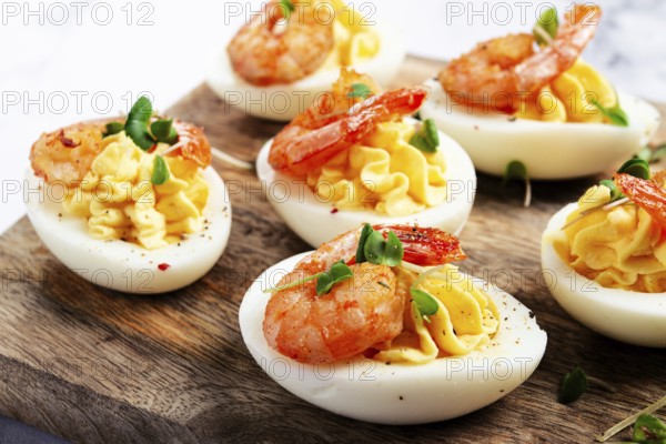Boiled eggs stuffed with yolk and seasoned with mayonnaise, stuffed eggs with shrimp, on a wooden chopping board, selective focus, close-up, no people