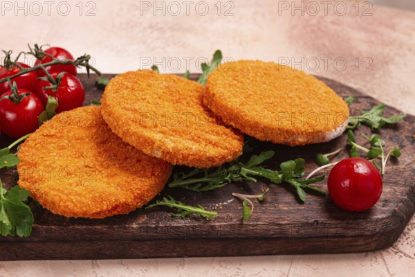 Crispy fried fish cutlets, fish burgers, on a wooden chopping board, with arugula and cherry tomatoes, homemade, no people