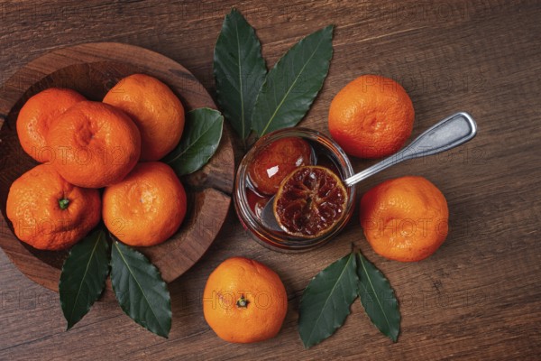 Jar of tangerine jam, stands on a wooden table, with fresh tangerines