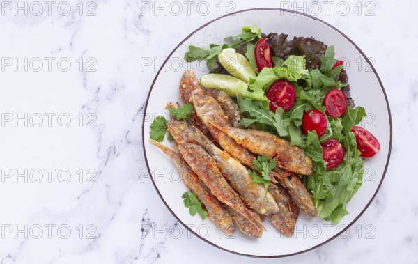 Fried crispy mullet fish, with fresh salad, on a plate with lime, no people
