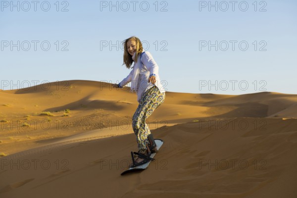 Young woman with snowboard in the sand dunes, near Merzouga, Meknès-Tafilalet region, Erg Chebbi, northern Sahara, Morocco