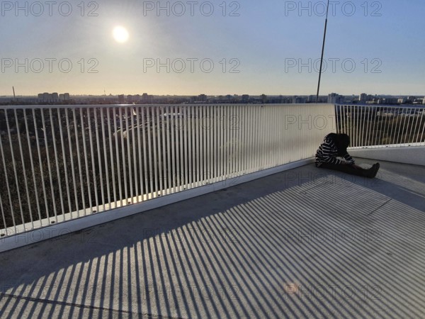 A person sitting alone on a railing with a view of an urban landscape at sunset, abstract, stripes, marzahn, Berlin