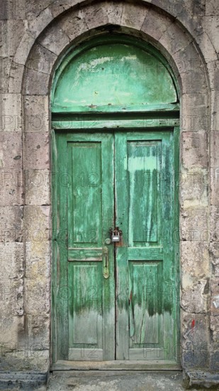 Locked green wooden door with a stone arch, rustic charm