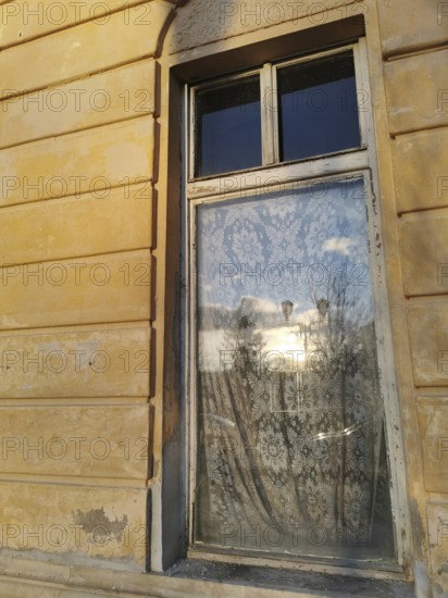 A window with a lace curtain reflecting the surrounding area on a sunny afternoon, Czech Republic