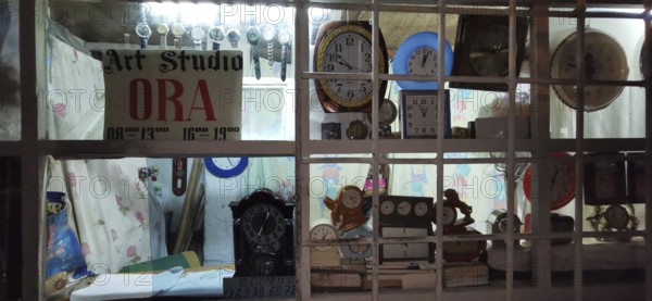 A shop window of an art workshop with various clocks and a sign, illuminated at night, Berat, Albania