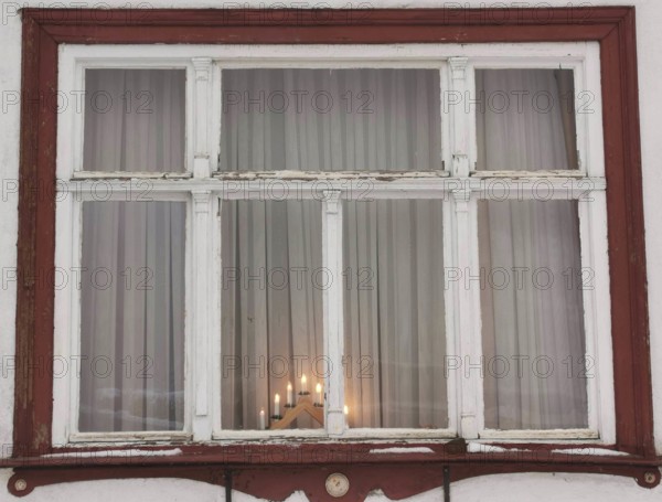 Rustic window with red wooden frame and candles inside, creates a cozy evening mood