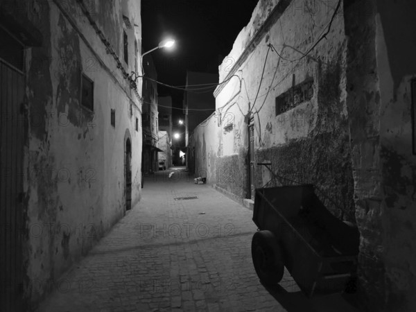 Abandoned old alley in nighttime darkness, faintly lit by black and white lanterns, Essaouira, Morocco