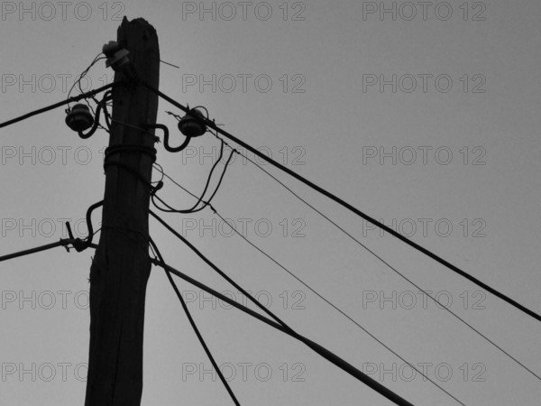 Close-up of an old wooden power pole with several wires against the sky, black and white, Berat, Albania