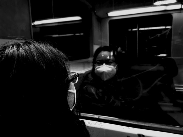 A person wearing a mask looks at their reflection in a train window during corona, black and white, Germany