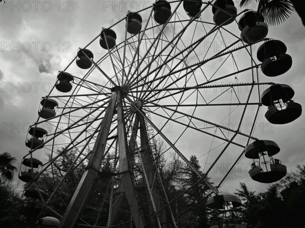 Silhouette of a Ferris wheel against a cloudy sky in a black and white theme park, Kutaisi, Georgia