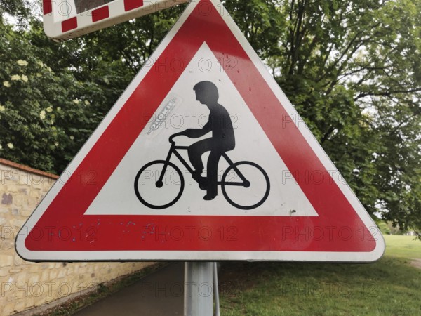 Road sign for bicycles, red and white triangle in the foreground, trees in the background, Czech Republic