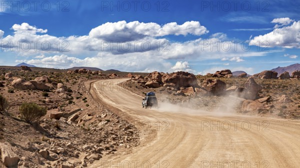 A vehicle drives on a dusty desert road through rocky landscapes under blue skies, The landscape of the Altiplano in Bolivia