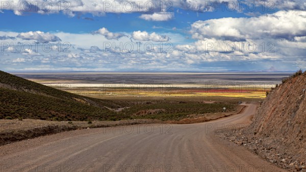 A dirt road leads through a vast, hilly landscape under a cloudy sky, The Landscape of the Altiplano in Bolivia